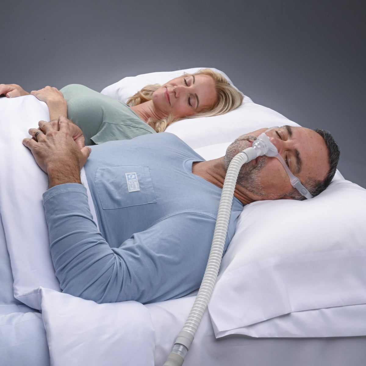Stock Image of Man Sleeping Supine Using REMSleep DeltaWave Nasal CPAP Mask W/ Headgear W/ Partner in Bed
