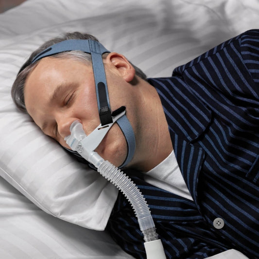 Stock photo of man sleeping while wearing Philips Respironics OptiLife nasal pillow CPAP mask with headgear