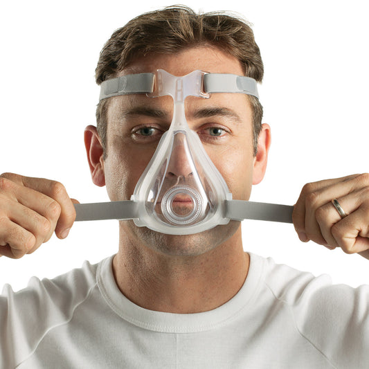 Forward facing man wearing ResMed Quattro Air full face CPAP mask tightening the headgear straps