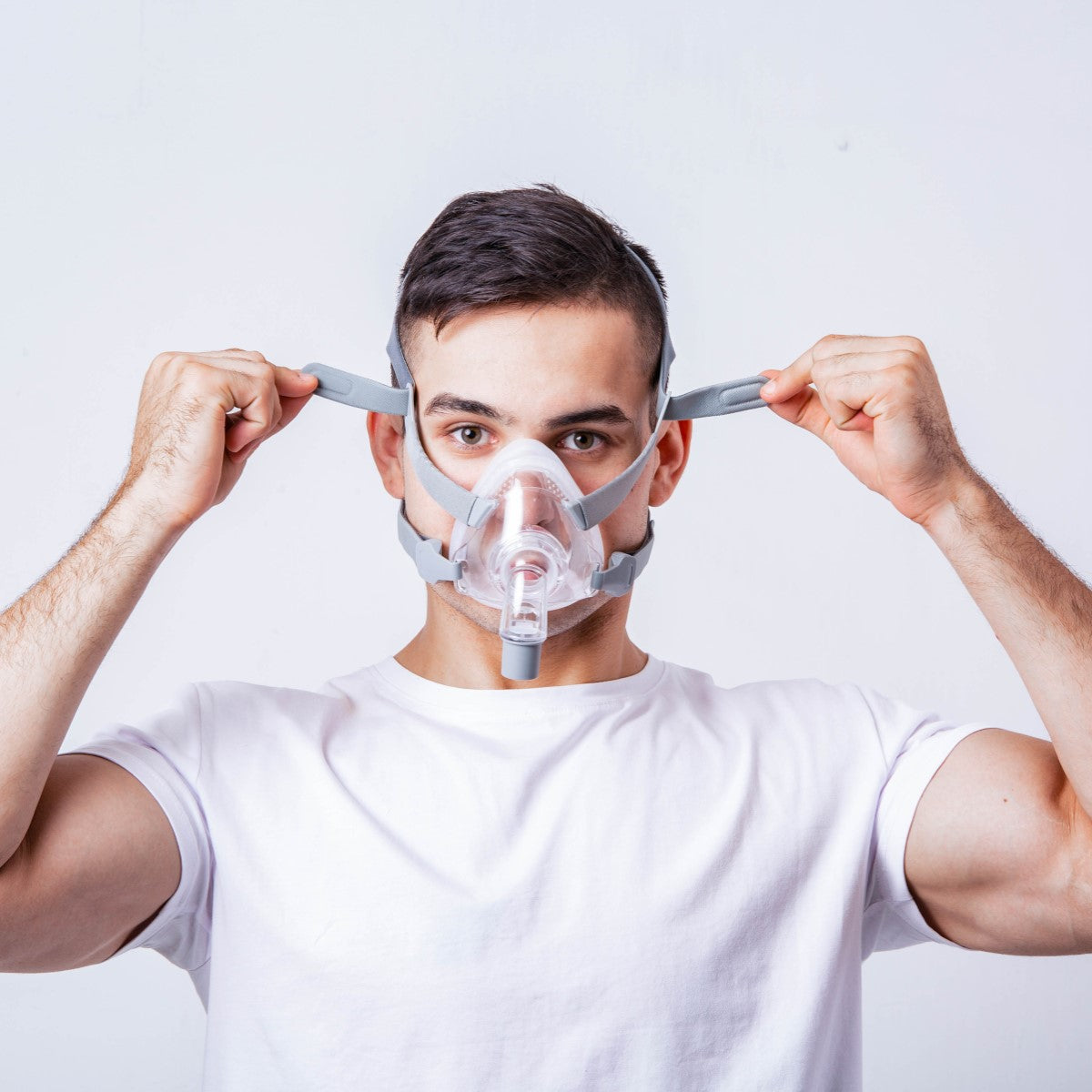 Stock Image of Man Placing React Health's Siesta Full Face CPAP Mask W/ Headgear on Face