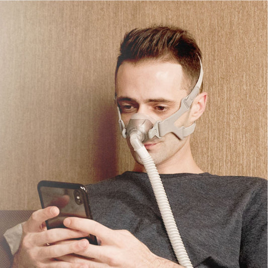 Man on his phone while wearing an Apex Medical Wizard 510 nasal CPAP mask system
