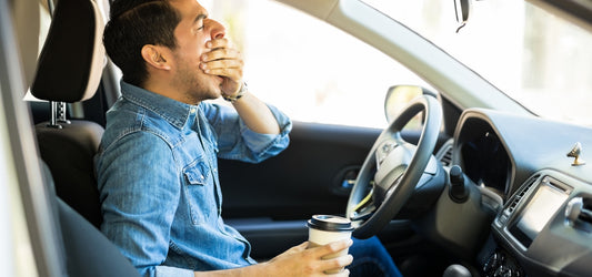 Man yawning in a car while holding a coffee cup.