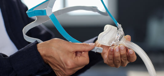 Person adjusting a CPAP machine mask and tubing for sleep apnea therapy.