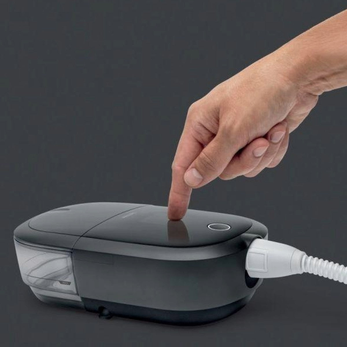 Hand pressing a button on a DreamStation 2 CPAP with a gray background