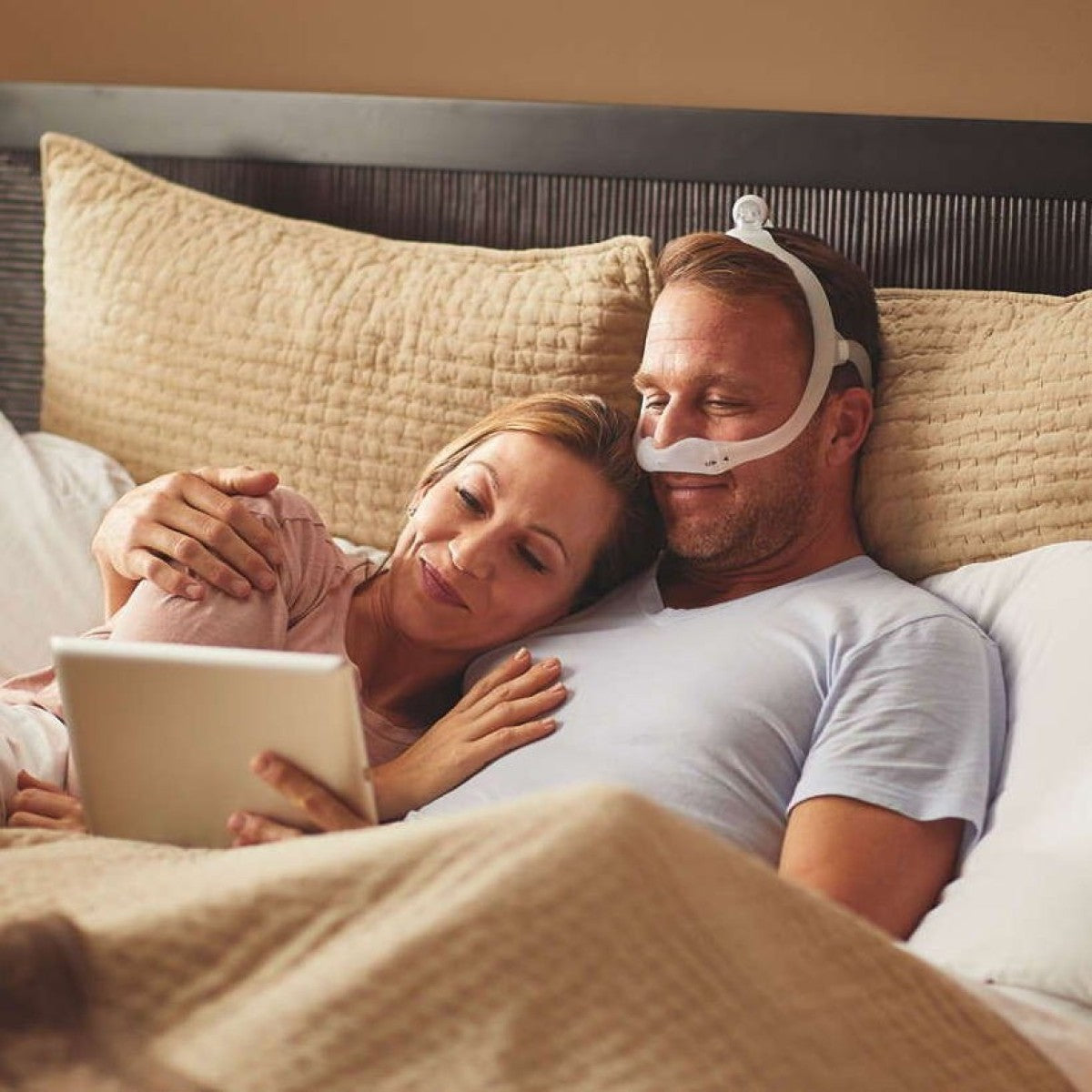 Man Wearing Philips Respironics DreamWear Nasal Mask W/ Headgear Laying Next to Woman in Bed