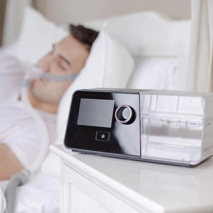 Person using a CPAP machine to sleep with a device on a nightstand.