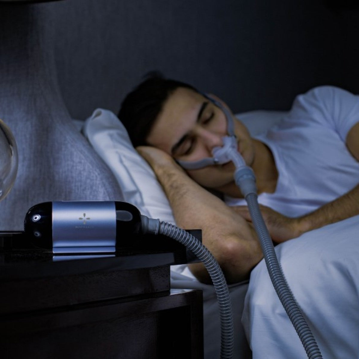 Person using a CPAP machine to sleep with a device on a nightstand.