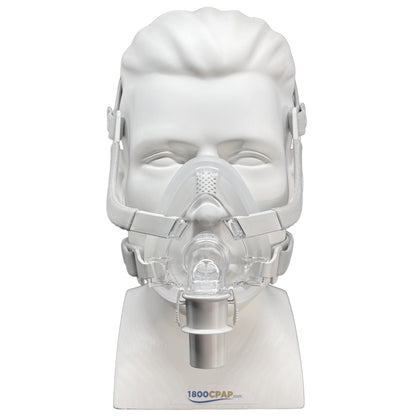 A clear CPAP mask displayed on a white mannequin head and stand against a white background. The mask has a clear facepiece, transparent headgear straps, and a silver valve connector.